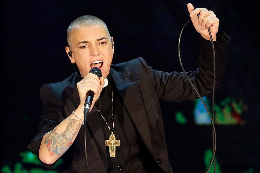 Sinead O'Connor dressed as a priest with a Buddism tattoo on her forearm
