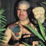Ozzy Osbourne shaved bald holding a machine gun