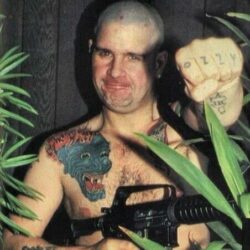 Ozzy Osbourne shaved bald holding a machine gun
